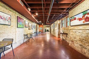 A corridor with brick walls, metal chairs, tables, and a mural on the right.