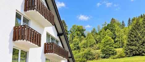 A multi-story building with balconies, a clear sky, and a green landscape.