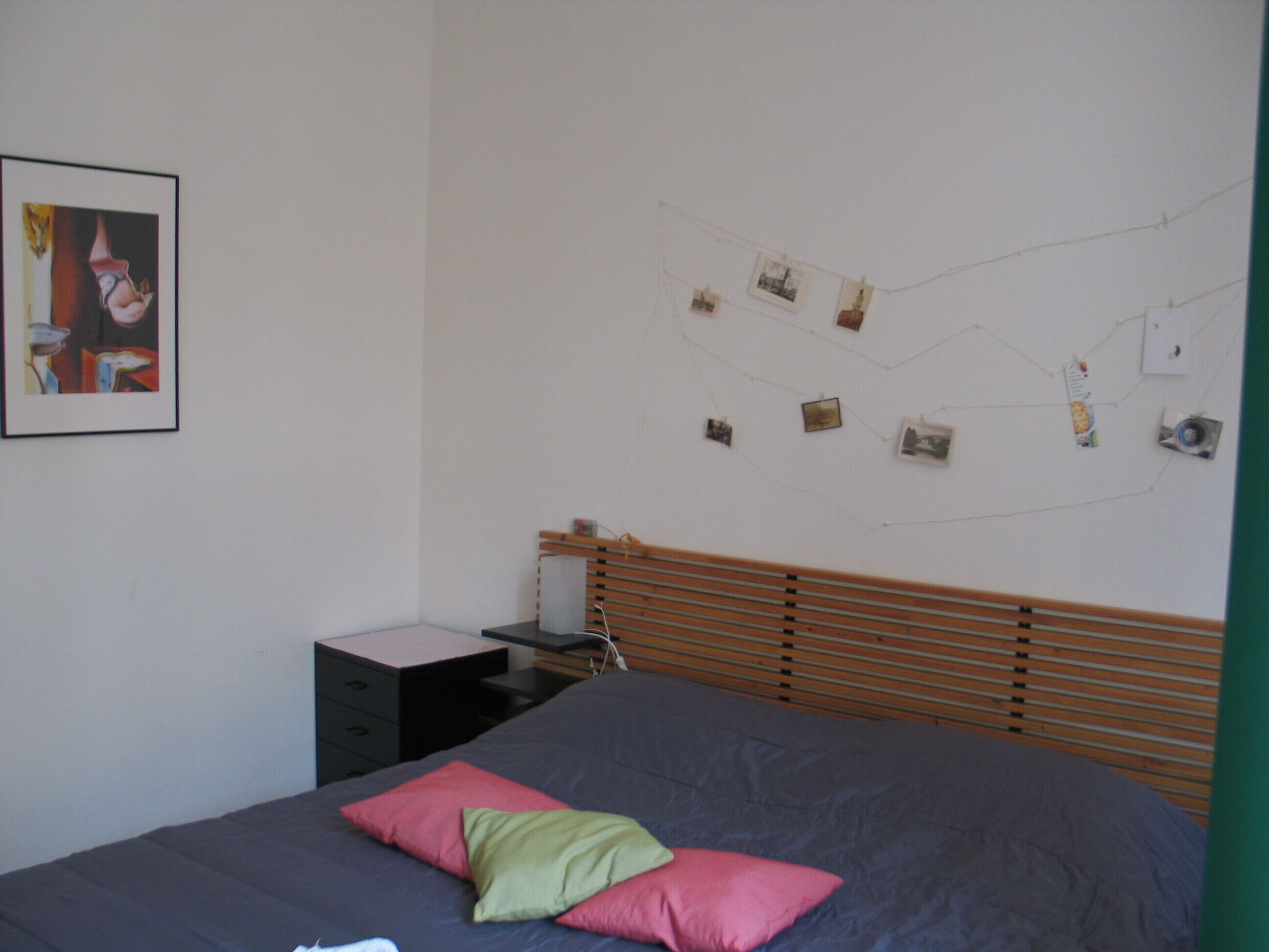 A bedroom with a bed, pillows, a nightstand, a dresser, and a wall with pictures.