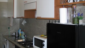 A compact kitchen with white cabinets, a black refrigerator, a microwave, and a sink. - Appartamentino vicino alla Stazione ed al Centro (Padova)
