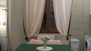 A small dining area with a table set for two, a window with curtains, a washing machine, and a radiator. - Appartamentino vicino alla Stazione ed al Centro (Padova)