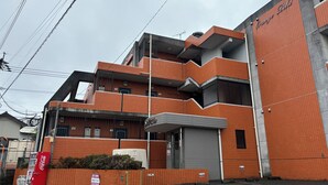 A multi-story building with orange tiled walls, a Coca-Cola vending machine, and a fenced area with mattresses. - 2 double beds, free Wi-fi, can accommodate up to 4 people 【ANY INN FUKUOKA NANAKUMA (福岡市)