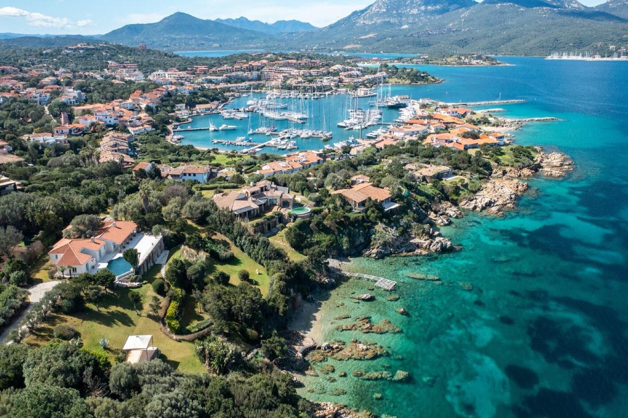 An aerial view of a coastal town with a marina, residential buildings, and clear turquoise waters.