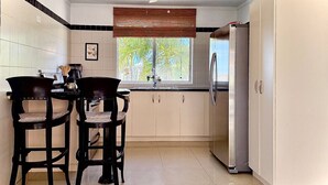 Une cuisine avec deux chaises en bois, une table à manger, un réfrigérateur et une fenêtre avec des stores.