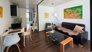 Ein modernes Wohnzimmer mit einem Glastisch, einem schwarzen Sofa und einem Essbereich mit einem weißen Stuhl.