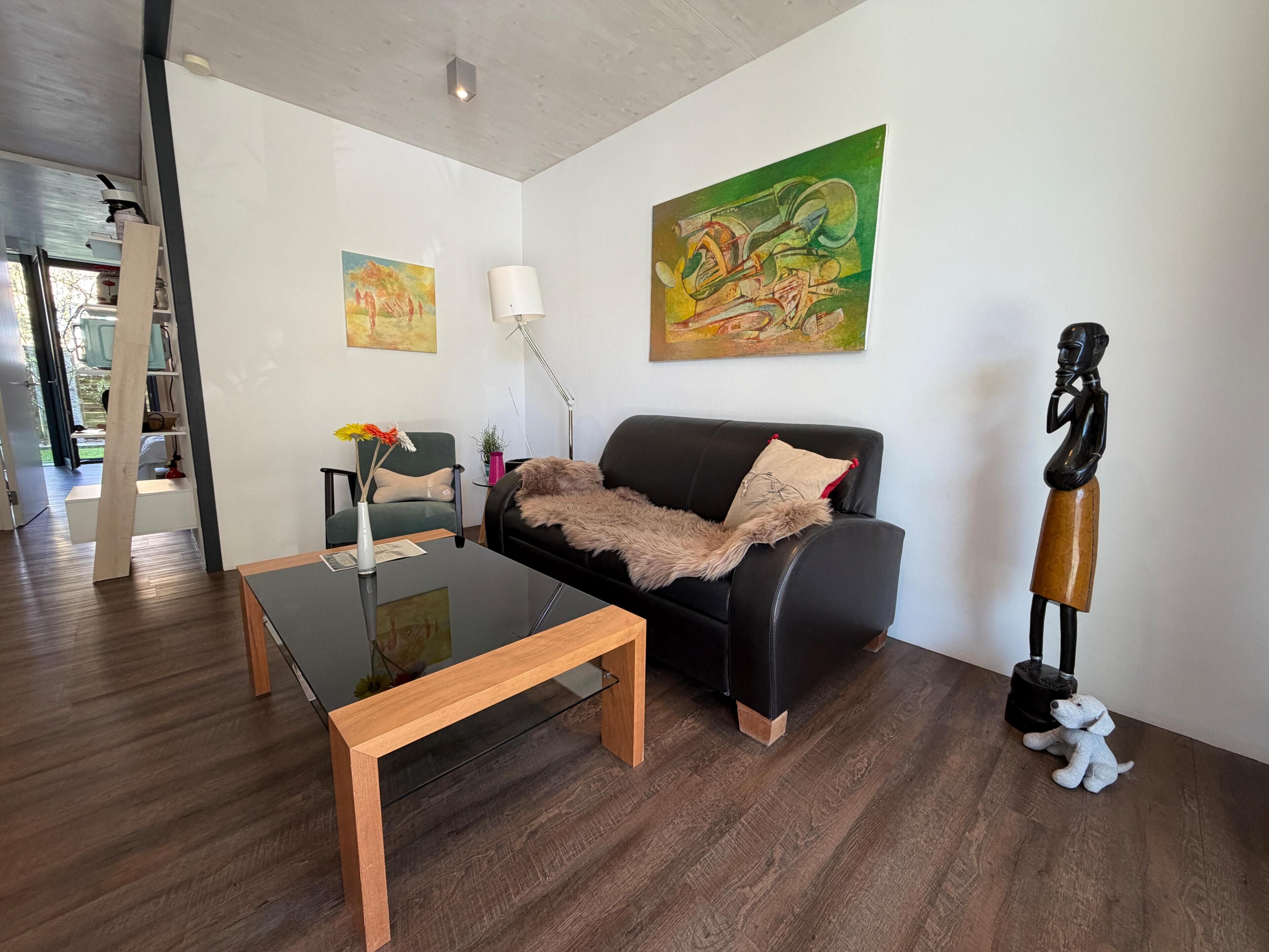 A modern living room with a black leather sofa, a glass coffee table, and a painting on the wall.