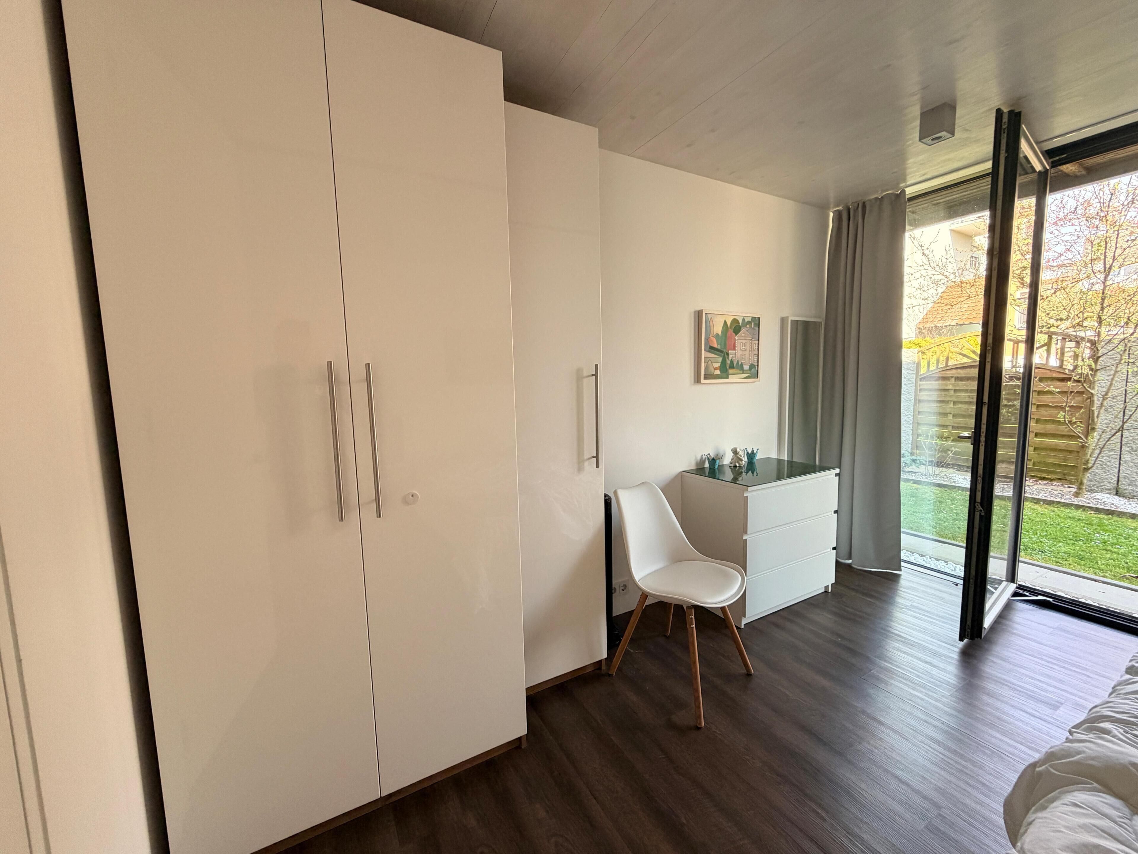 A modern bedroom with a large wardrobe, a desk with drawers, a chair, and a bed.