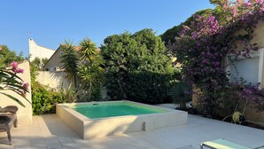 A rectangular swimming pool with a tiled deck, surrounded by lush greenery and flowering plants. - Vacation home with pool (Agde)