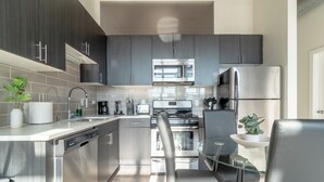 Una cocina moderna con electrodomésticos de acero inoxidable, armarios oscuros y una mesa de comedor de vidrio.