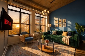 Een woonkamer met een groene bank, een blauwe fauteuil, een salontafel en een televisie waarop het Netflix-logo te zien is.