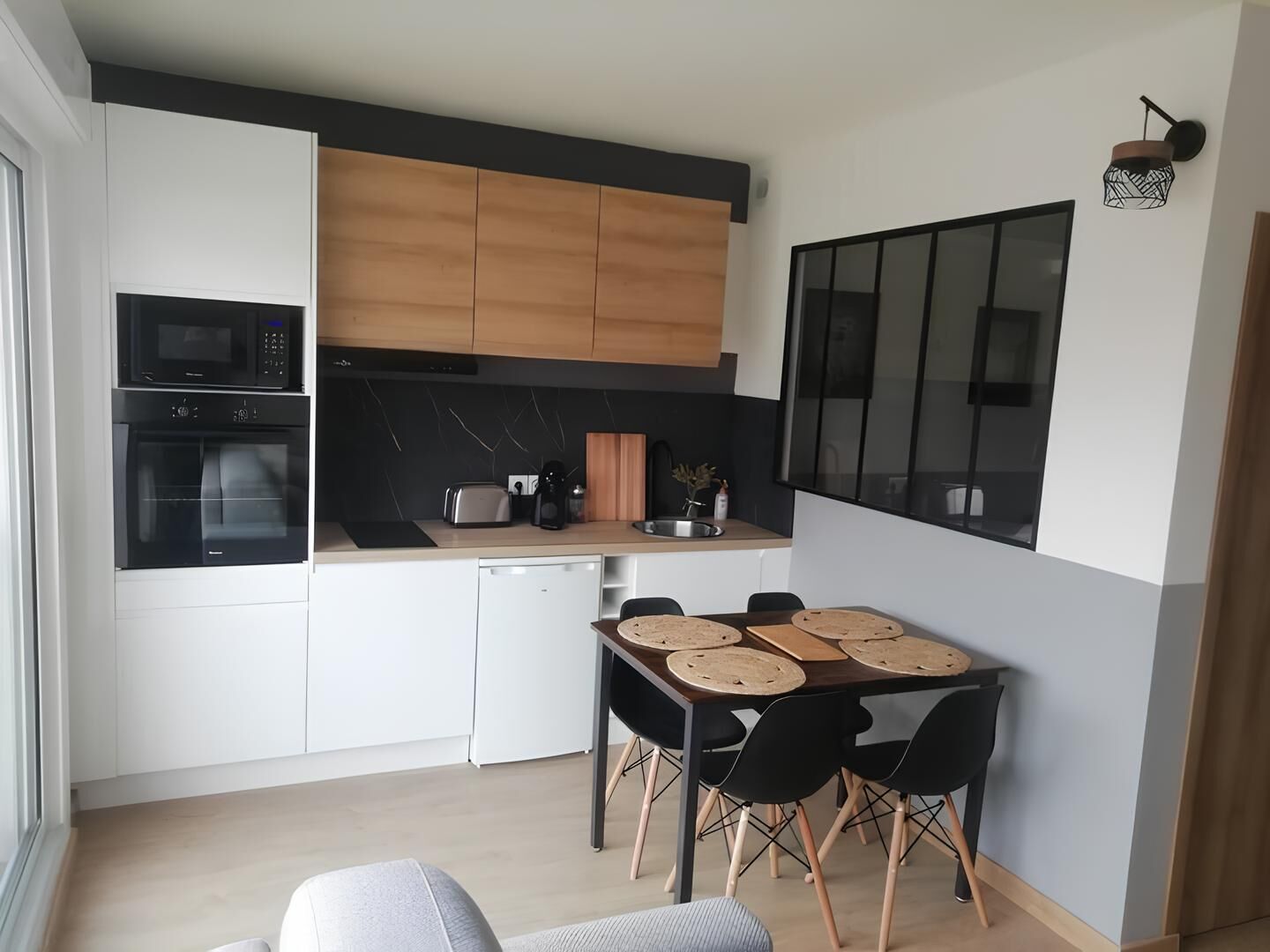 Une cuisine compacte avec des meubles blancs, un plan de travail noir et un coin repas comprenant une table et des chaises.