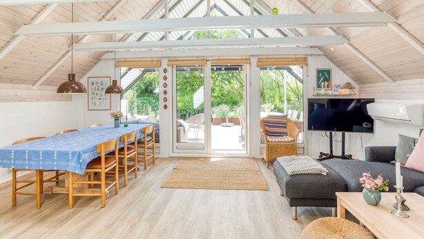 A spacious room with a high ceiling, a dining area with a table and chairs, a sofa, a TV, and a large window providing a view of the outdoors. - "Frodde" - 200m from the sea by Interhome (Sydals)