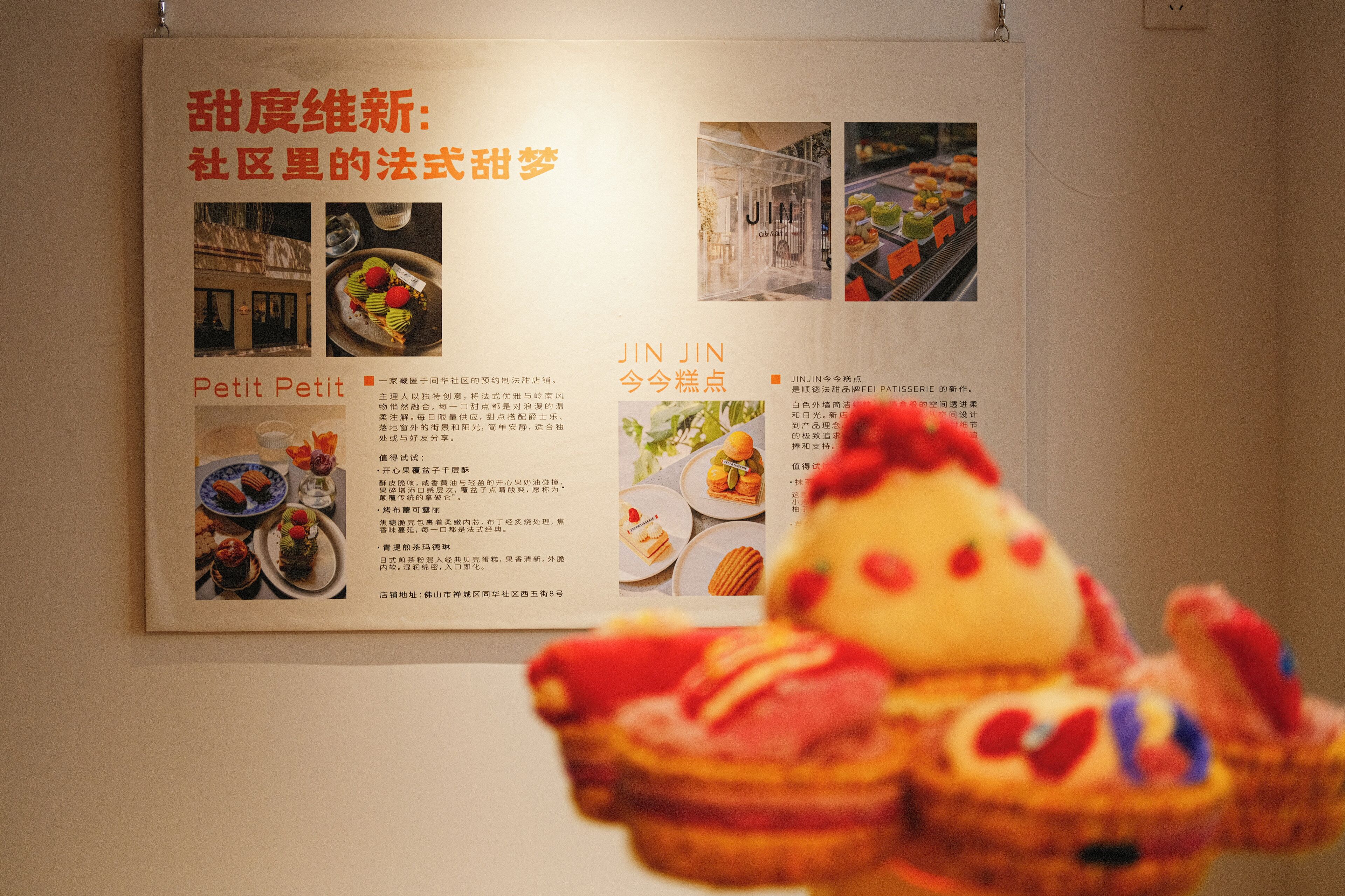 A menu board with food images and descriptions, a plush toy in the foreground, and a wall-mounted light fixture.