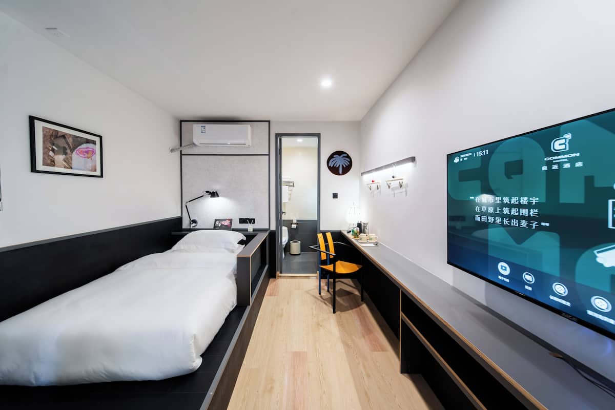 Une chambre d’hôtel moderne équipée d’un lit, d’un bureau, d’une chaise et d’un grand écran de télévision affichant des informations sur la chambre.