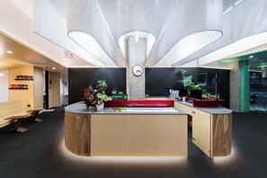 A modern reception desk with a clock, potted plants, and a sign indicating breakfast. - CommonHotel (Foshan)