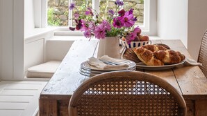Un coin repas avec une table en bois, une chaise en osier et une fenêtre donnant sur un paysage verdoyant.