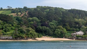Un paysage côtier avec une plage de sable, un petit bateau et une maison située près de l’eau.