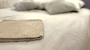 A neatly made bed with a folded blanket in the foreground, a headboard, and a wall-mounted light fixture.