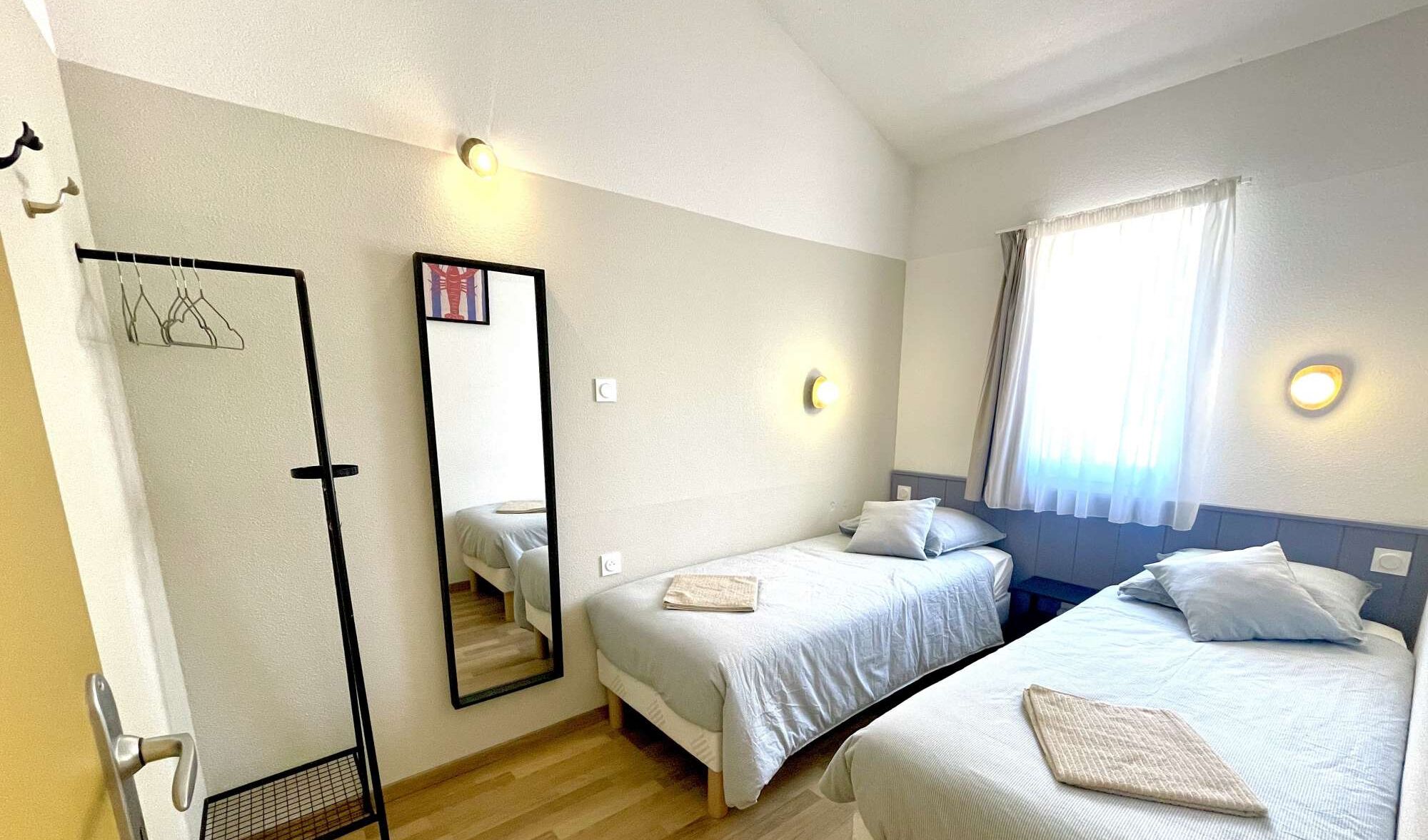 Ett hotellrum med två sängar, en spegel och ett fönster med gardiner.