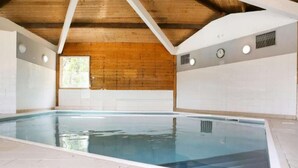 An indoor swimming pool with a wooden ceiling and white tiled walls.