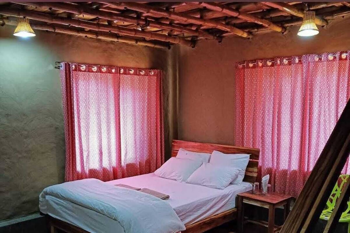 A bedroom with a wooden bed, red patterned curtains, and a wooden floor.
