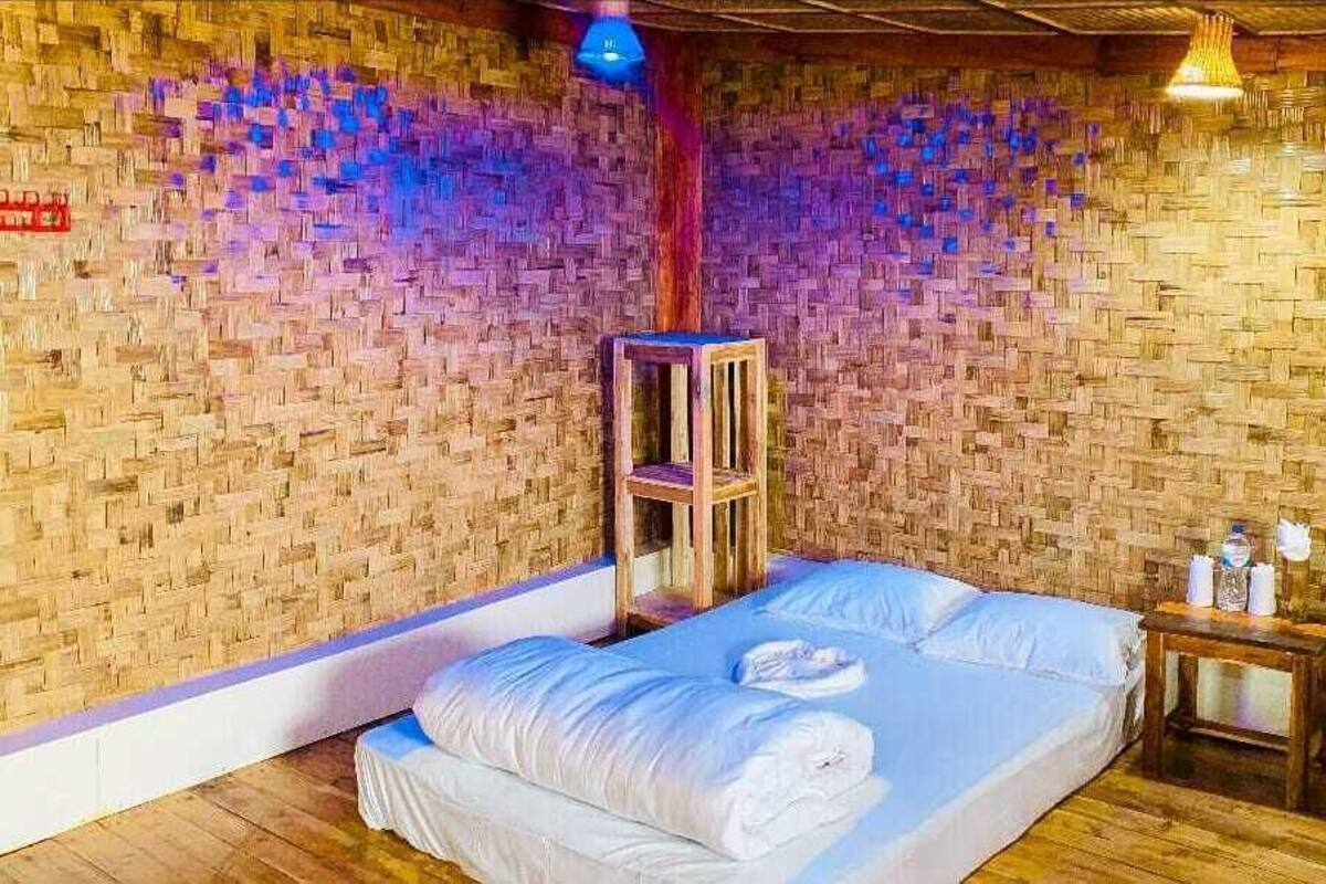 A room with a woven wall, a bed with white linens, a wooden nightstand, and a hanging light fixture.