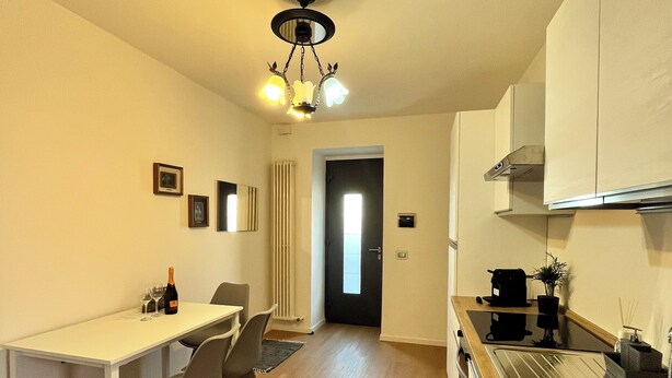 A compact kitchen with a dining area, a white table, and chairs. There is a bottle of wine and glasses on the table. - La Rosa - Comfort & Charm in the Town Center (Monselice)