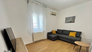 A modern living room with a sectional sofa, a small round table, and a flat-screen TV on a wooden stand. - La Rosa - Comfort & Charm in the Town Center (Monselice)