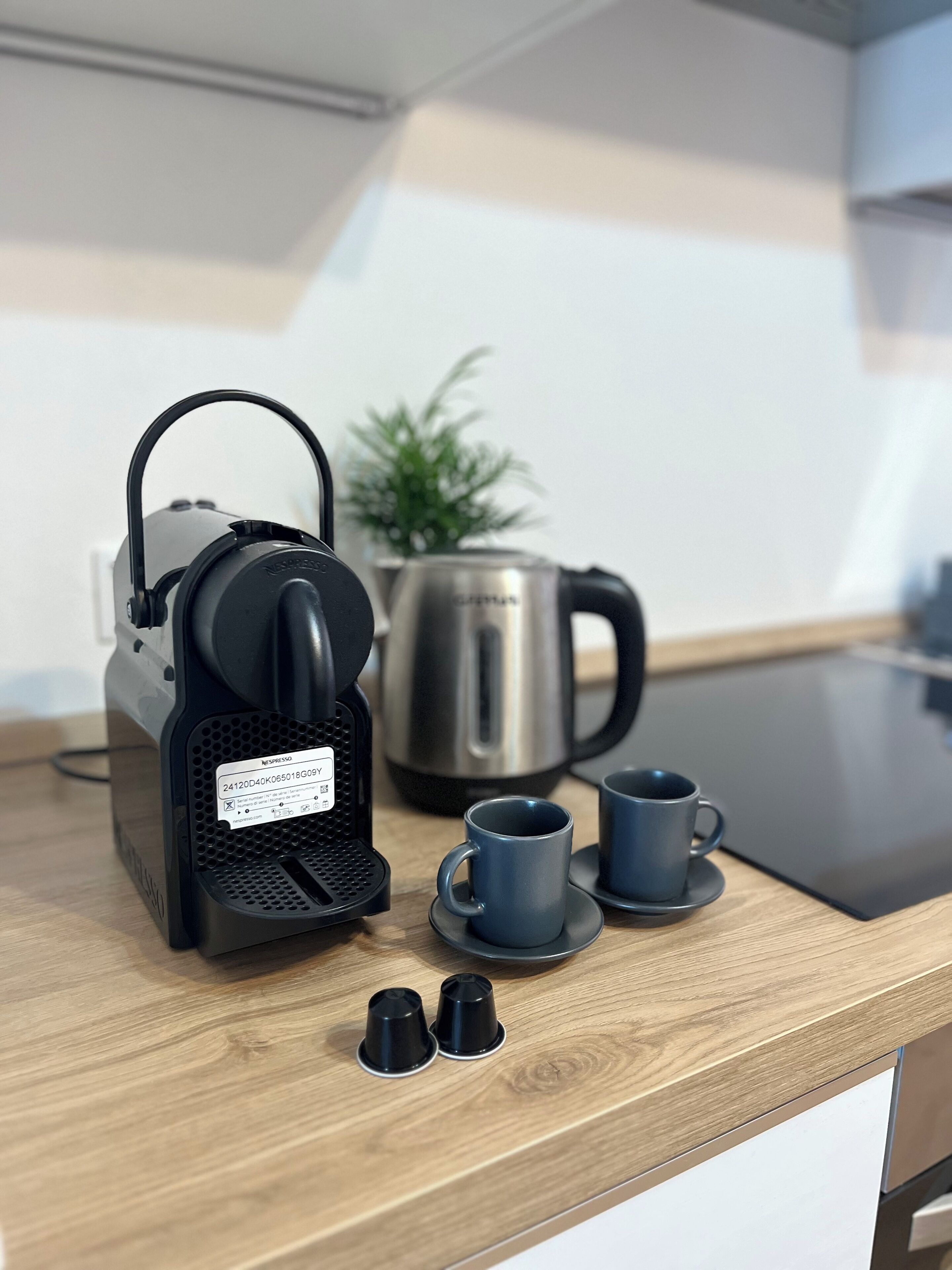 Una encimera de cocina con una máquina de café Nespresso, una tetera de acero inoxidable y dos tazas azules.