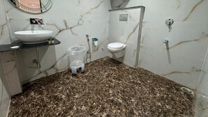 A bathroom with a marble floor, a sink, a toilet, and a hand dryer. - Velora Inn  (Varanasi)