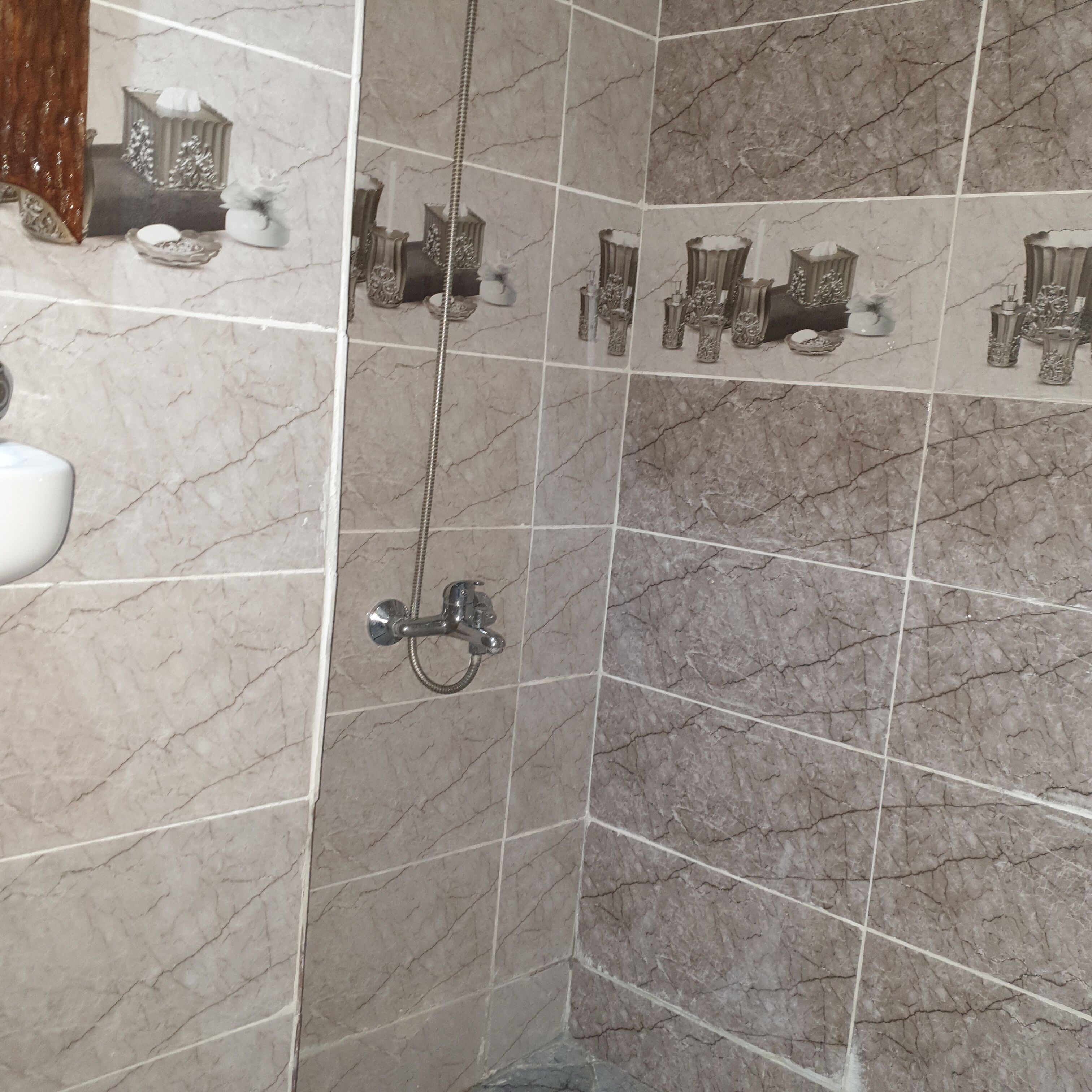 Un baño con ducha, paredes de azulejos y suelo de mármol.