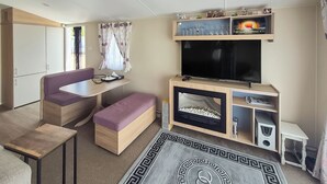 A compact living space with a dining area, a sofa, a TV, and a fireplace. - 3 bedroom accommodation in Hayling Island (Hayling Island)