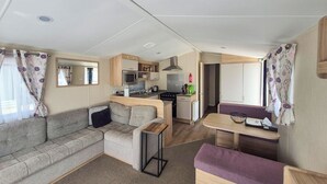 A compact RV interior with a kitchenette, a sofa, a dining table, and a small bench. - 3 bedroom accommodation in Hayling Island (Hayling Island)