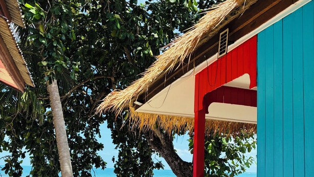 Una escalera junto a la playa con barandillas rojas que conduce a un edificio azul con techo de paja.