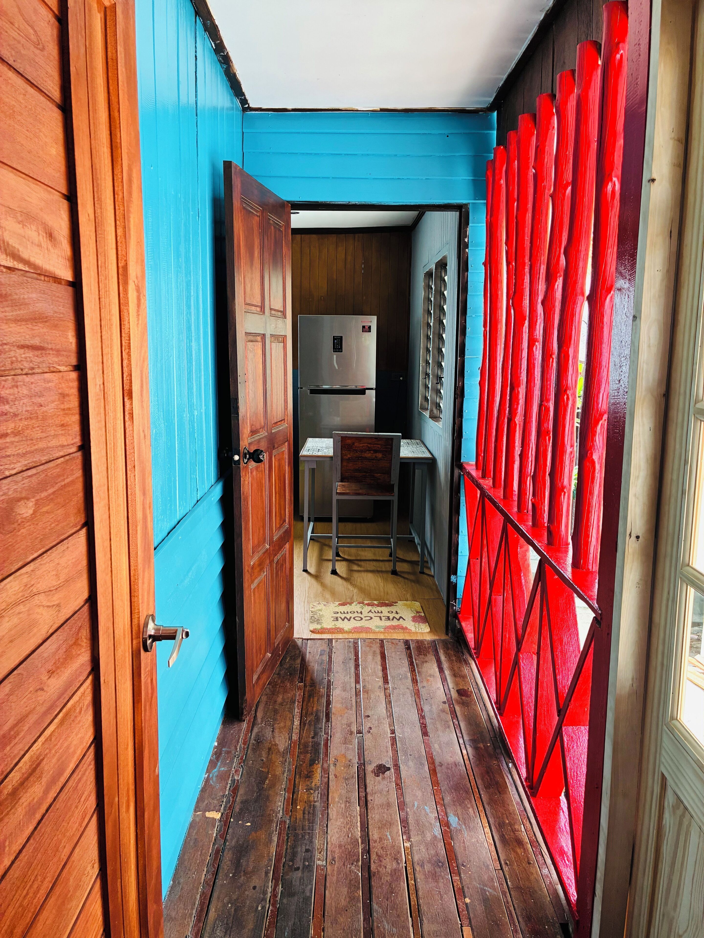 Un pasillo estrecho con suelo de madera, pared azul y barandilla roja.