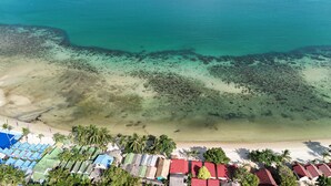 An aerial view of a beach resort with multiple bungalow-style buildings, a sandy beach, and a clear turquoise sea. - Lamai Beachfront Bungalow Koh-Rooms (Koh Samui)