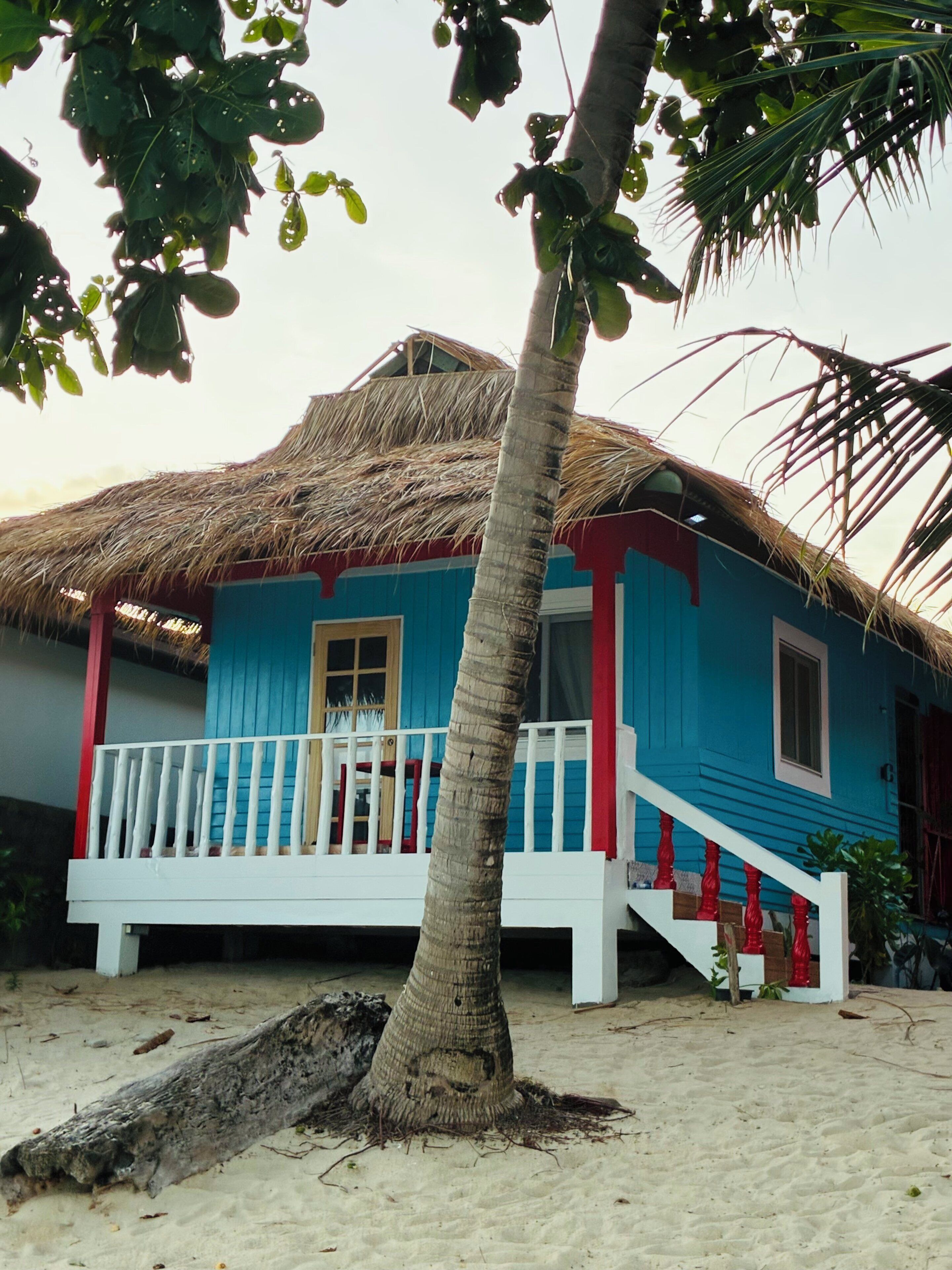 A beach house with a thatched roof, a blue exterior, and a white porch.