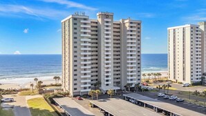 A high-rise hotel with multiple balconies, a parking area, and a view of the ocean.