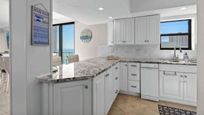 A modern kitchen with white cabinetry, a marble countertop, and a large window providing a view of the city.