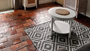 Une pièce avec un meuble blanc, un téléviseur fixé au-dessus d’une fenêtre et un tapis à motifs sur le sol.
