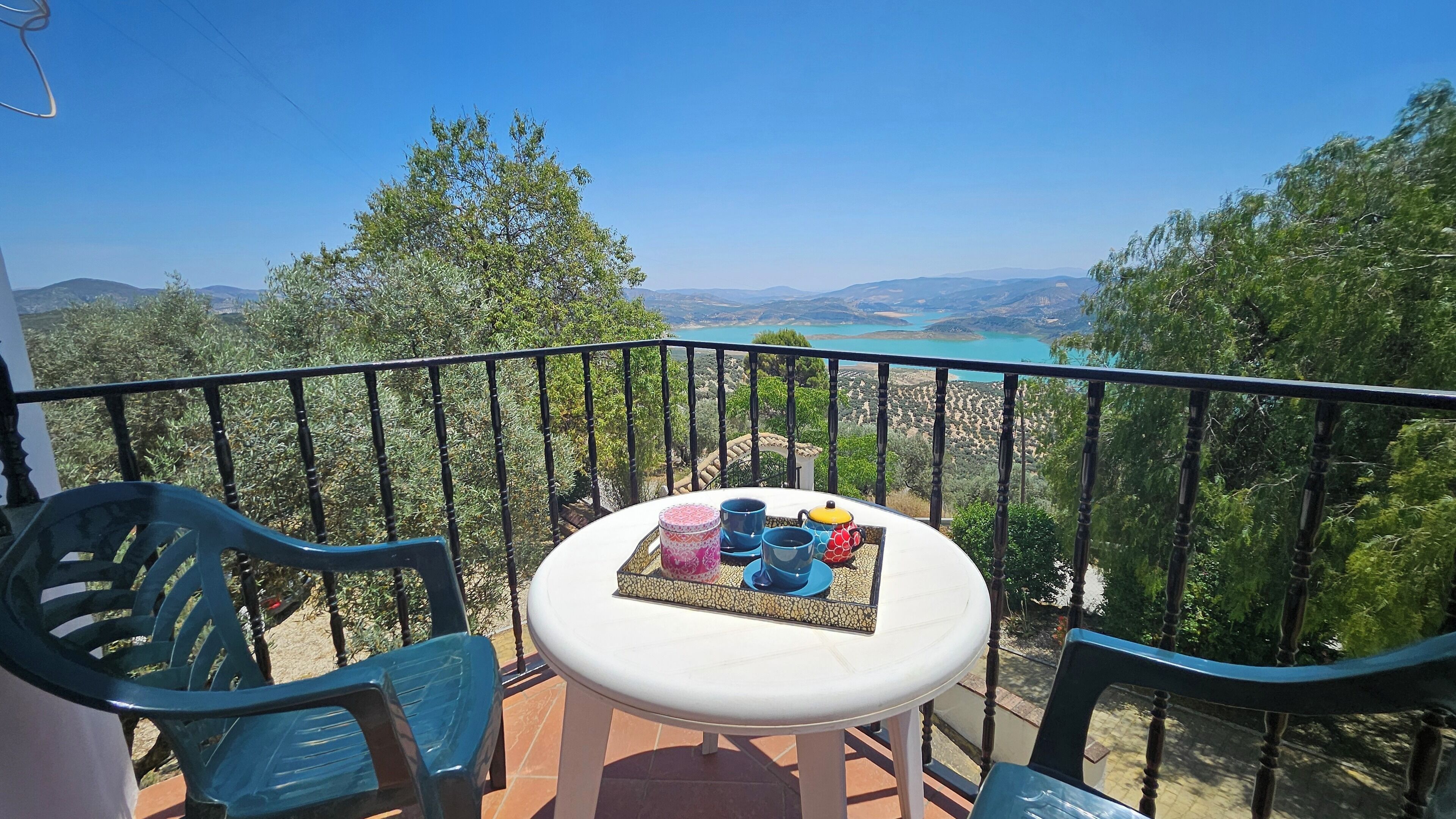 Varanda com mesa posta para chá, com vista para uma paisagem cênica, árvores e um lago ao longe.