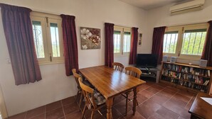 A dining area with a wooden table and chairs, a television, and a bookshelf with books.