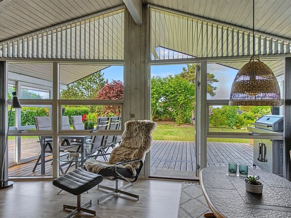 Un intĂ©rieur moderne avec de grandes fenĂȘtres, un coin repas et un fauteuil lounge.