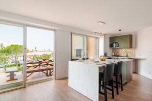Una cucina moderna con una grande isola, porte scorrevoli in vetro che si aprono su un balcone e vista sul mare.