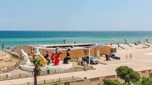Blick auf einen Strand mit einem Gebäude, bunten Skulpturen und einem strahlend blauen Himmel.