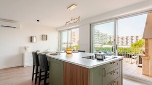 Eine moderne Küche mit einer großen Kochinsel, Barhocker, Blick auf die Stadt und einem Balkon mit Geländer.