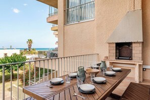 Un balcone con tavolo apparecchiato per mangiare, affacciato su una spiaggia e l'oceano.