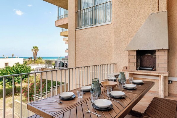 Un balcón con mesa lista para comer, con vista a una playa y al océano.