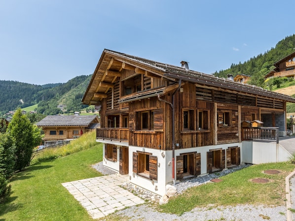 Eine Holzhütte mit Balkon, einem Steinweg und Blick auf die umliegenden Hügel.