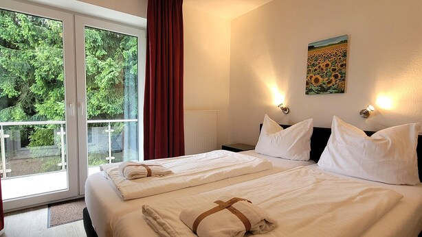 Une chambre d’hôtel avec un grand lit, un tableau au mur et une vue sur la verdure par la fenêtre.